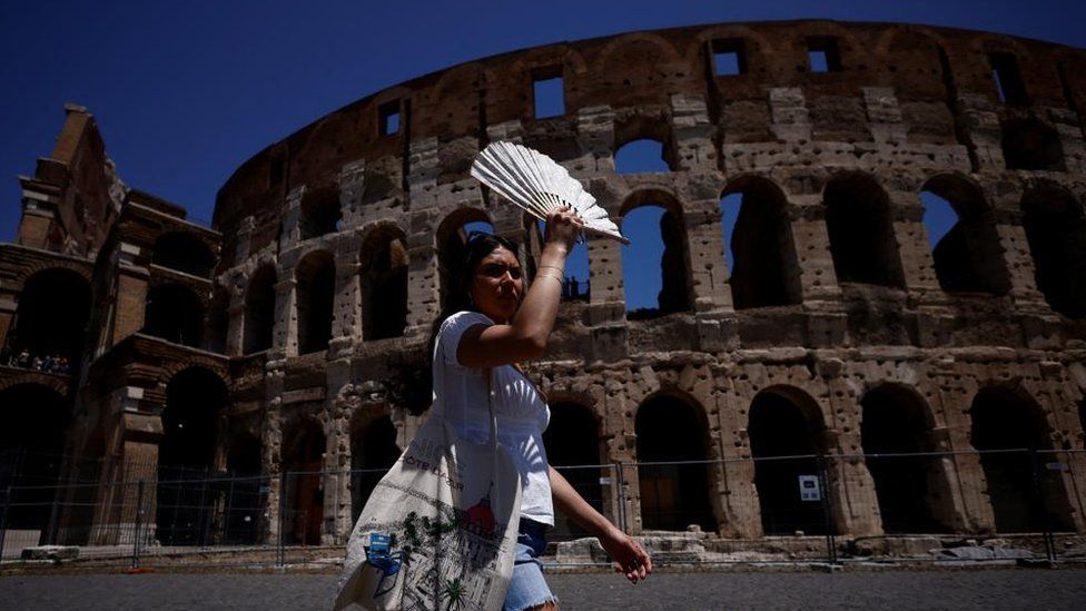 A pistillate   uses a instrumentality   to structure  from the prima   during a heatwave successful  Italy. The Colosseum is disposable   successful  the background.