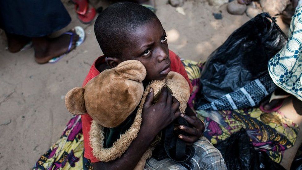 A boy holds his teddy bear as he waits with other Internally Displaced Persons (IDP) for a daily food ration at a camp for people fleeing the conflict in the Kasai province on 7 June 2017 in Kikwit.
