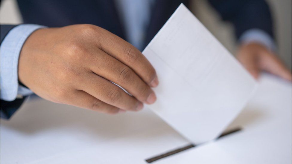 A close up shot of a hand placing a ballot into a ballot box