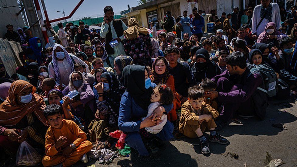 Women and children wait outside the Taliban controlled check point near the entrance of the airport in Kabul, Afghanistan