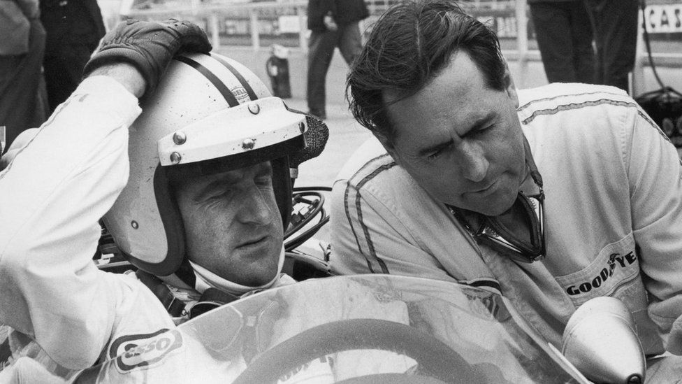 New Zealand racing driver Denny Hulme (1936 - 1992, left) confers with his team mate, Australian racing driver Jack Brabham before a practice run for the British Grand Prix at Silverstone, 13th July 1967.