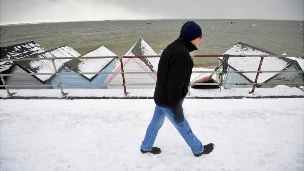 A man walks on the snow covered seafront at Thorpe Bay, Essex,