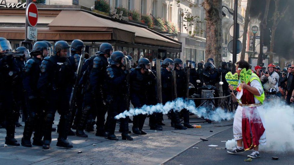 A line of riot police firing tear gas at a protester
