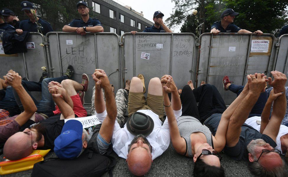 Protesters hold hands while lying on the ground during a demonstration in front of the Sejm building in Warsaw, Poland, 20 July 2017
