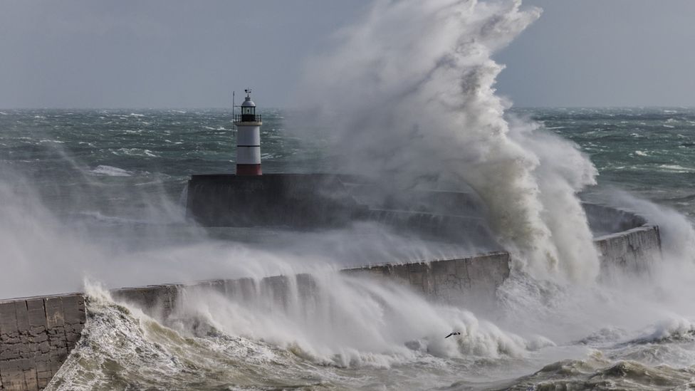 Stormy seas with sea water breaking over a sea wall near a lighthouse