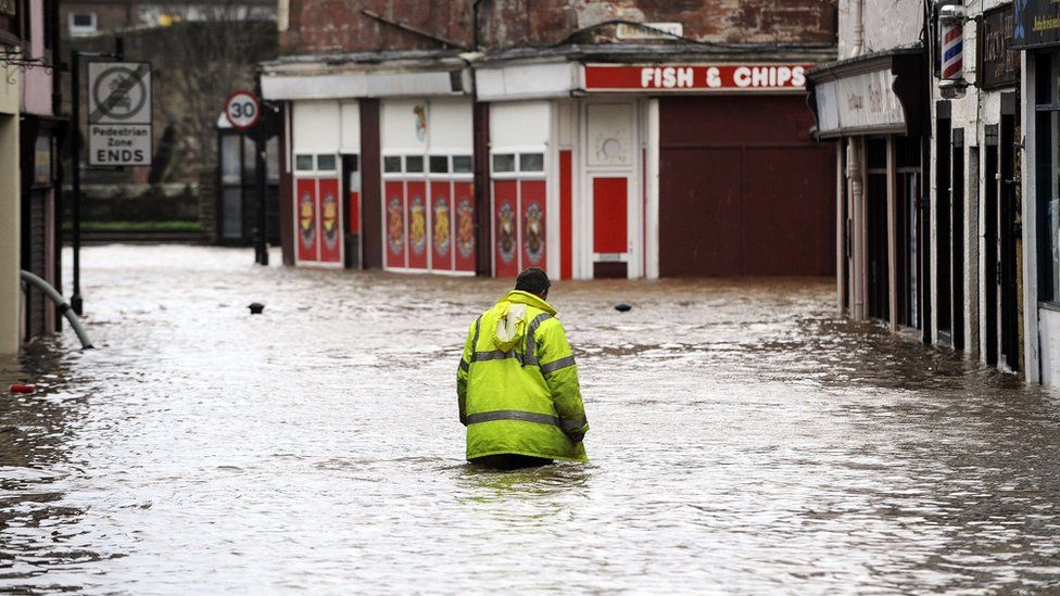 A man wades through floodwater in a street in Dumfries