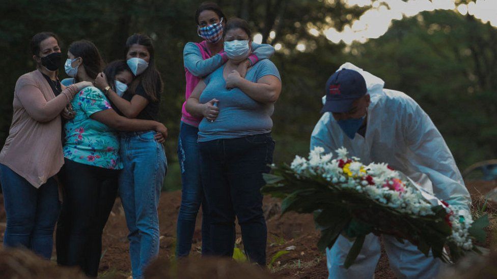 Родственники жертвы коронавируса скорбят, когда их любимый человек похоронен на кладбище Вила-Формоза в Сан-Паулу, Бразилия, 31 марта 2021 г.