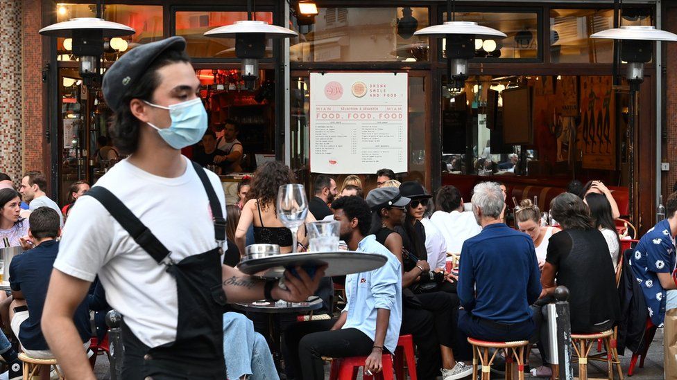 A waiter wearing a face mask serves clients while people eat and have drinks