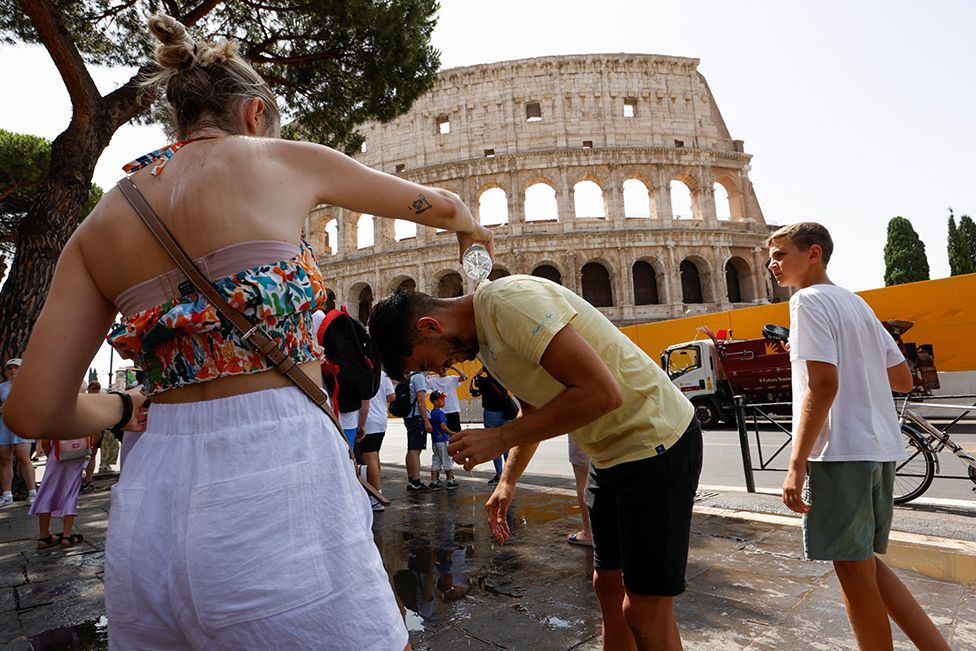 Женщина поливает мужчину водой возле Колизея в Риме, Италия