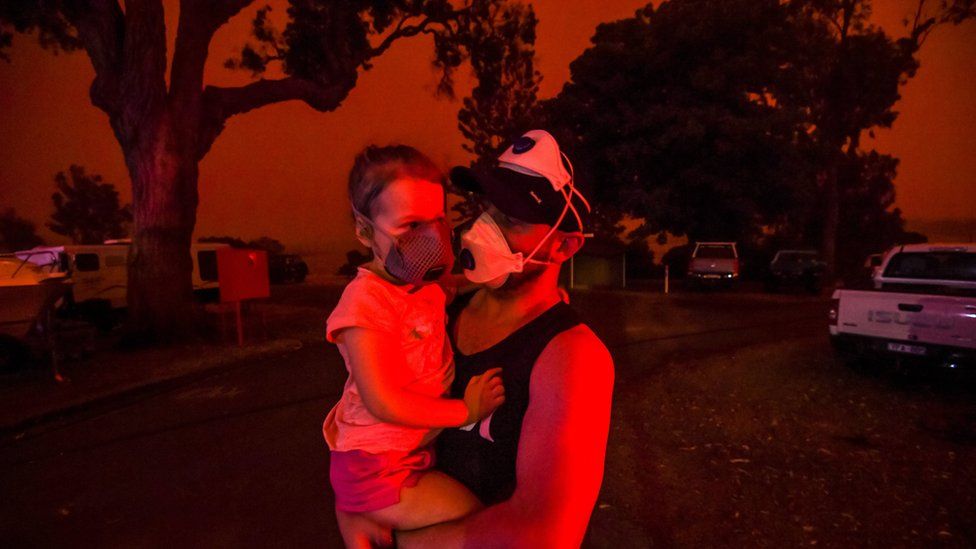 Mike hold his daughter Ella as the skies above turn red during the day on January 4, 2020 in Mallacoota, Australia