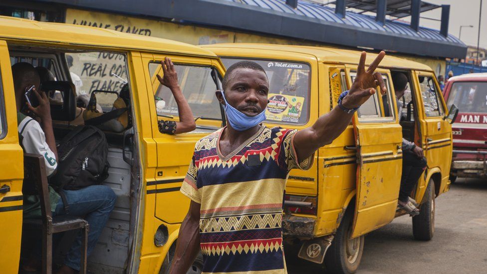 A conductor stands in front of a Lagos danfo