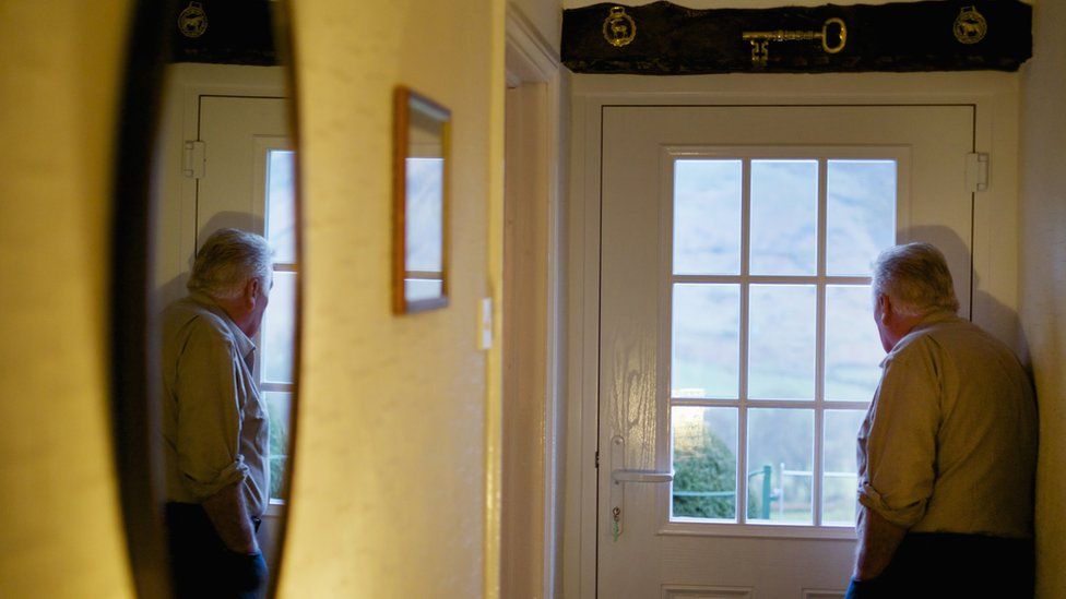 Elderly man looking out of his front door