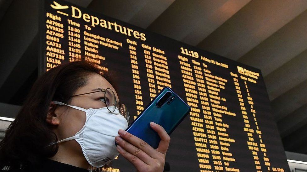 Une passagère portant un masque respiratoire parle sur son smartphone par le tableau des départs le 31 janvier 2020 à l'aéroport de Rome Fiumicino