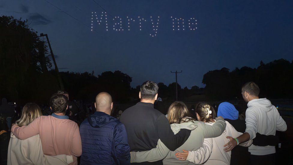 Rhys Whelan, Megan Greenwood and friends look at the words "marry me" in the sky