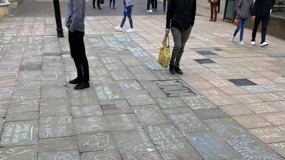 People walking and standing on High Street where there are chalk messages on the pavement