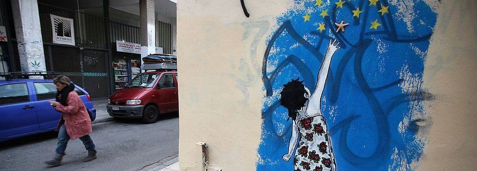 A woman walks past graffiti depicting a young girl trying to reach stars from the EU flag on 18 February 2012 in Athens, Greece