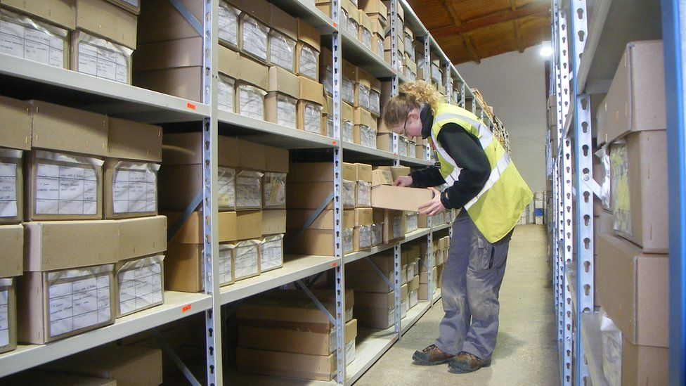 Storage racks with boxes with a worker attending to them holding a clipboard