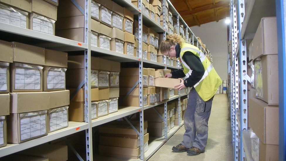 Estanterías de almacenamiento con cajas y un trabajador atendiéndolas con un portapapeles