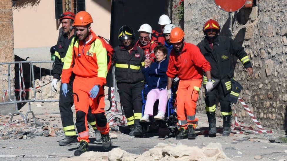 A woman on a wheelchair is carried away by rescuers in Norcia, central Italy