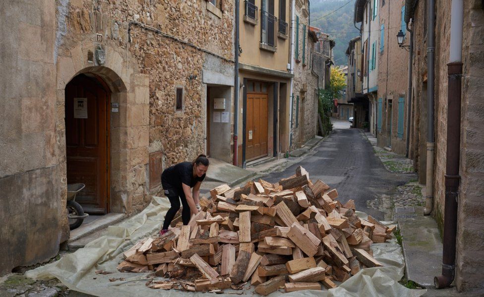 A woman and a pile of wood in a street in Alet-les-Bains
