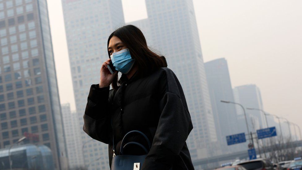 A woman wearing a mask to protect herself from pollutants walks past office buildings shrouded with pollution haze in Beijing, Monday, Dec. 7, 2015