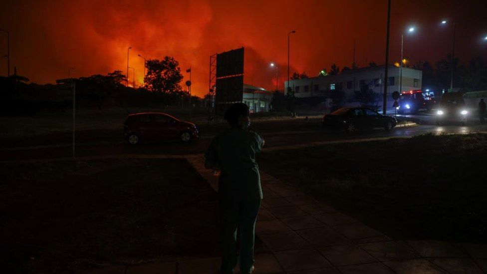 A nurse watches a wildfire burning near a hospital in Alexandroupolis, in the region of Evros, Greece