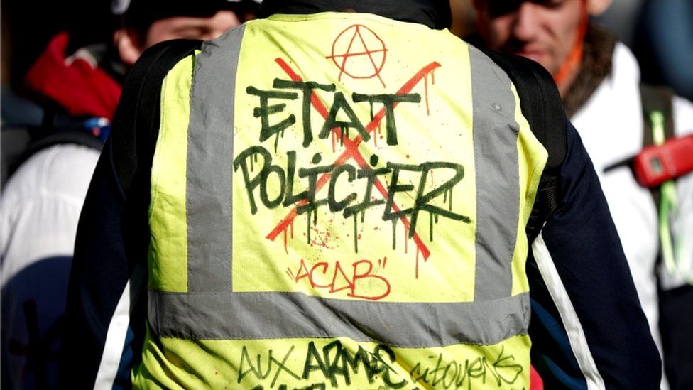 A protester's back with "police state" marked on vest