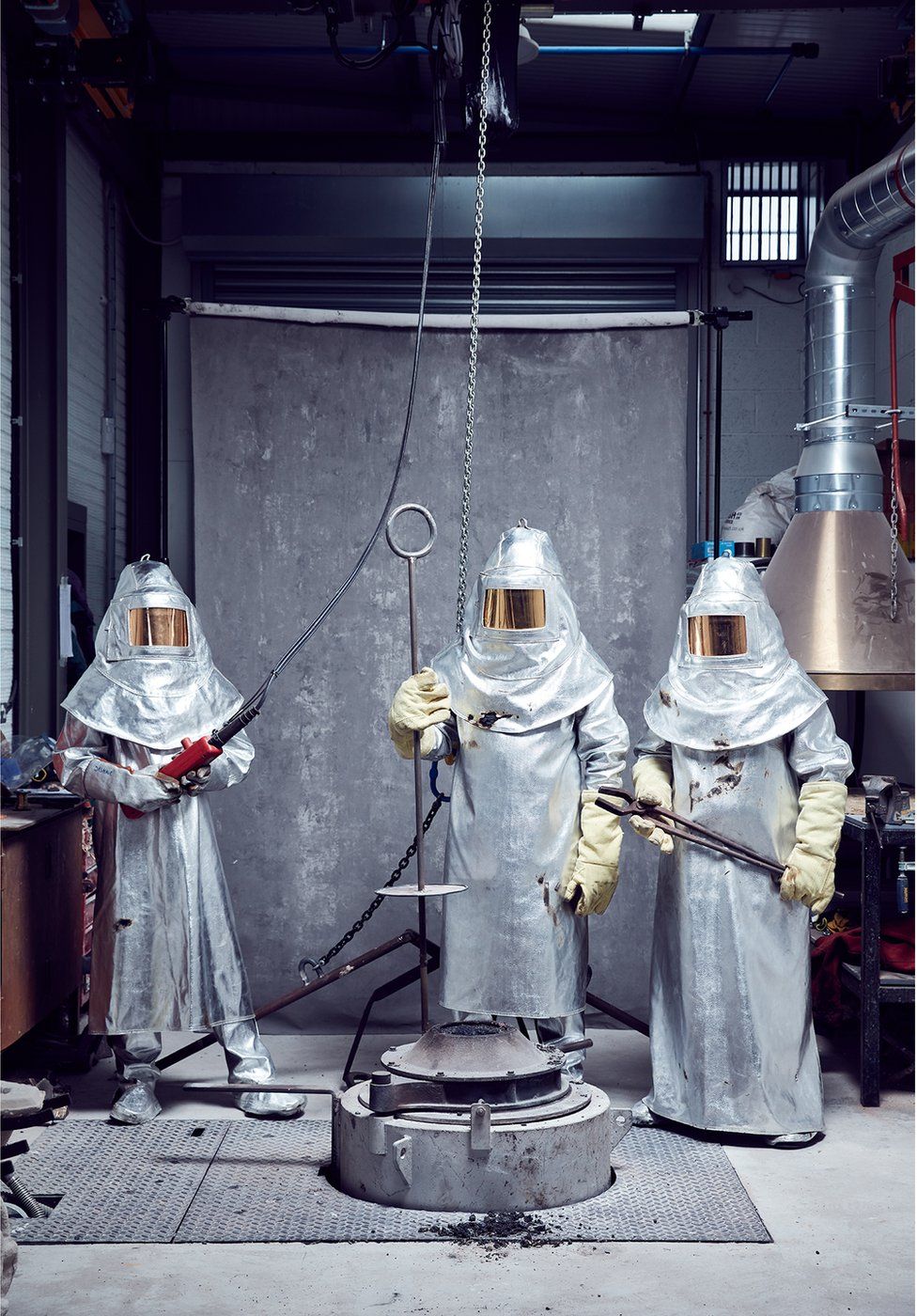 Three metal forgers stand in their protective equipment