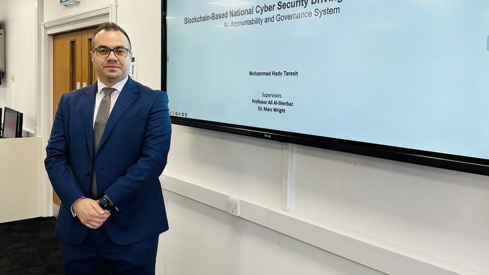 Mohamed Hady standing in front of a cyber security presentation