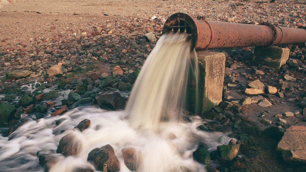 Wastewater flowing from a rusty pipe onto a river bank