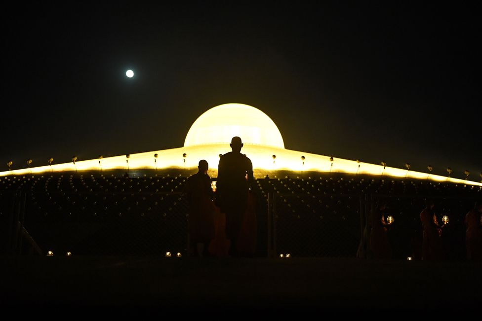 Buddhist monks carrying lit candles while the full moon rises during prayers to mark Makha Bucha Day at the Wat Phra Dhammakaya temple, near Bangkok.