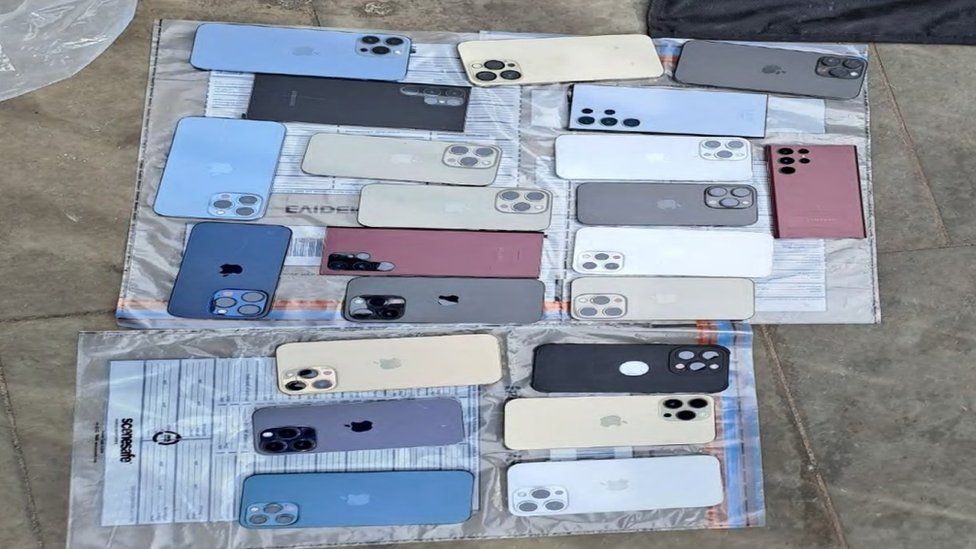 An image of 13 red, blue white and black mobile phones on top of evidence bags