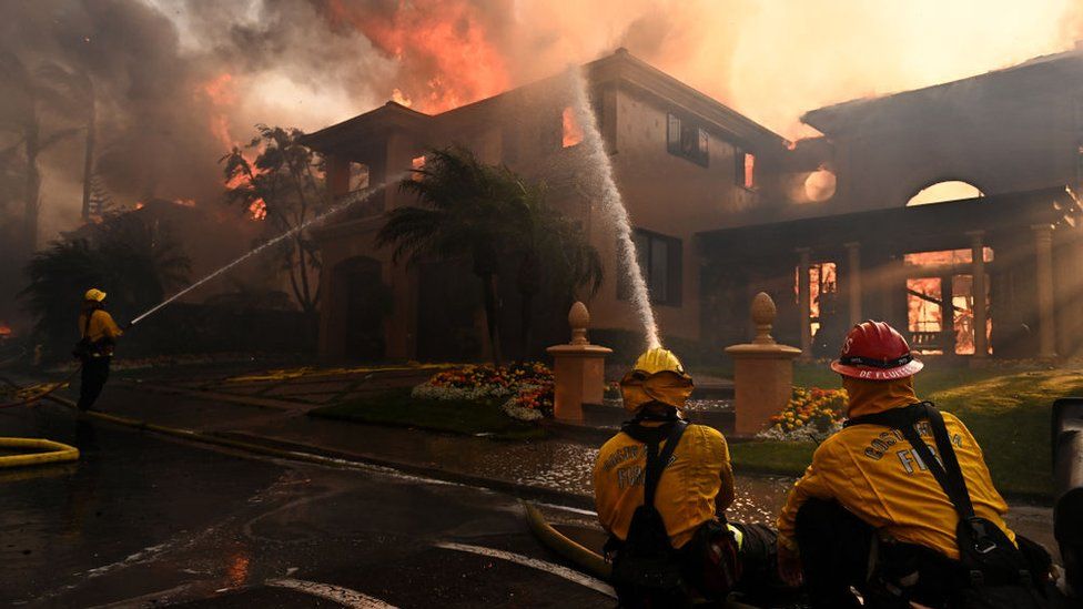 A mansion burning as firefighters try to put it out
