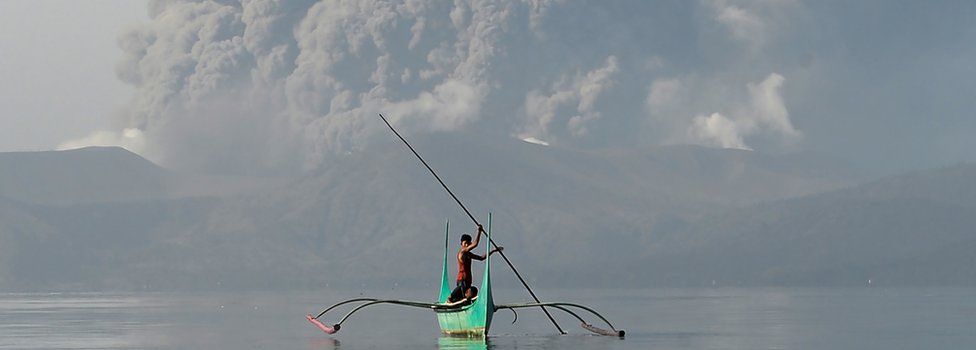 Small boat on Lake Taal with Taal volcano erupting behind