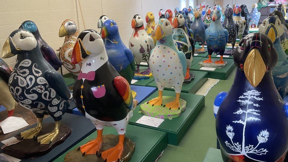 Decorated puffin statues in rows indoors