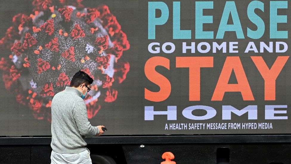A man wearing a mask walks past a billboard in Melbourne which reads: Please go home and stay home