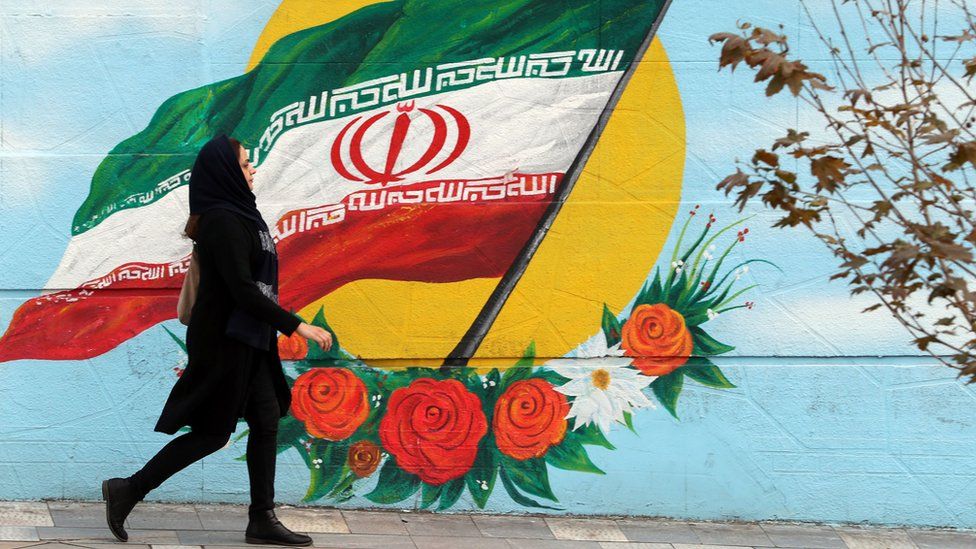 A woman walking in front of a mural featuring the Iran flag