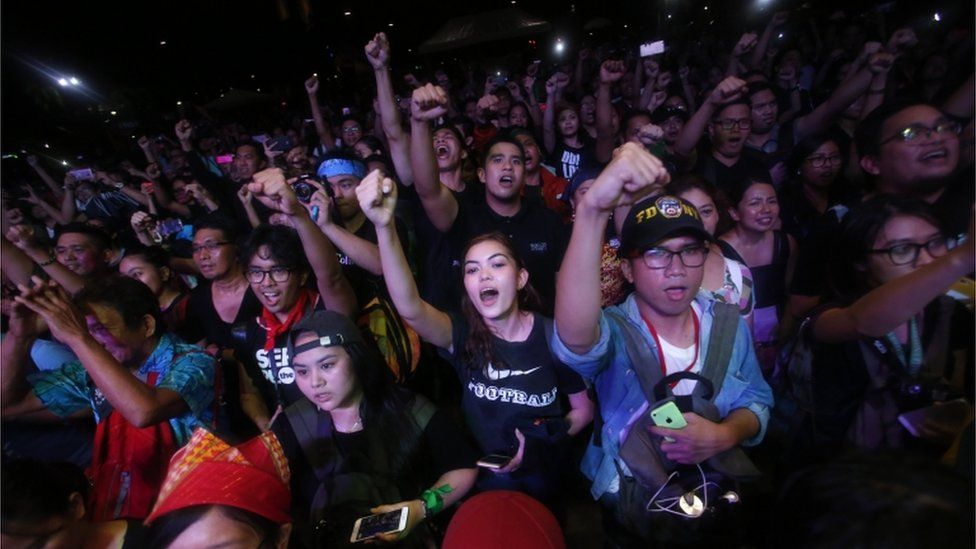 Young people are pictured holding hands up at a night time protest in Manila
