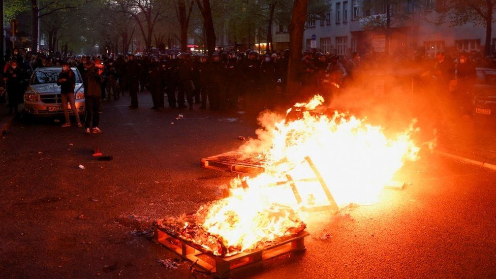 Police officers look on behind burning objects during a left-wing May Day demonstration in Berlin