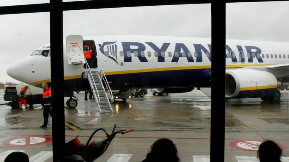 Travellers wait in front of a passenger jet belonging to Ryanair