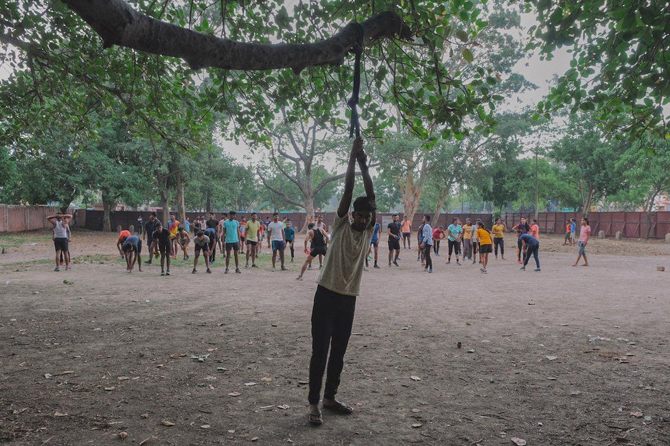 Under a large banyan tree young men train for physical tests for the defence exams