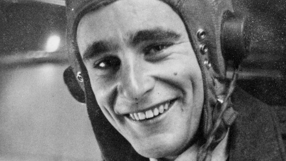 Black and white photograph of World War Two aircraft navigator Robert Seymour who is wearing a fabric aviator helmet with built-in headphones and smiling at the camera