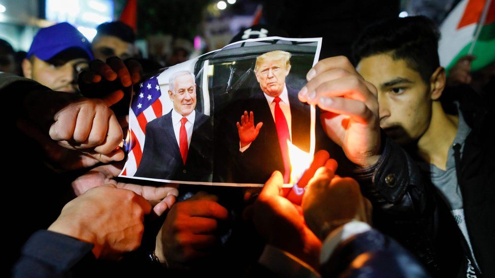 Palestinian protesters burn pictures of US President Donald Trump and Israel's Prime Minister Benjamin Netanyahu during a demonstration in the West Bank city of Ramallah