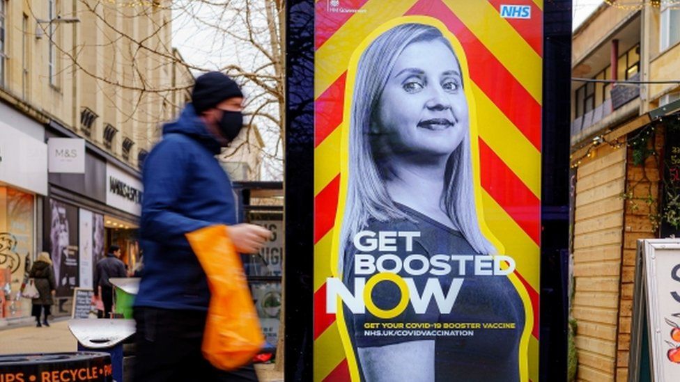 Man walks past a billboard for NHS Covid boosters