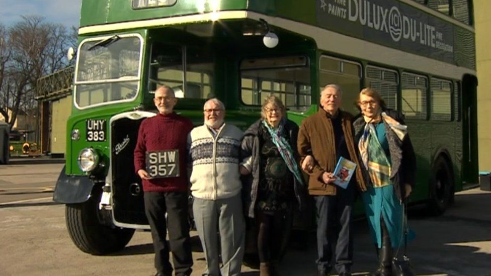 The five remaining adventurers standing by a green replica bus