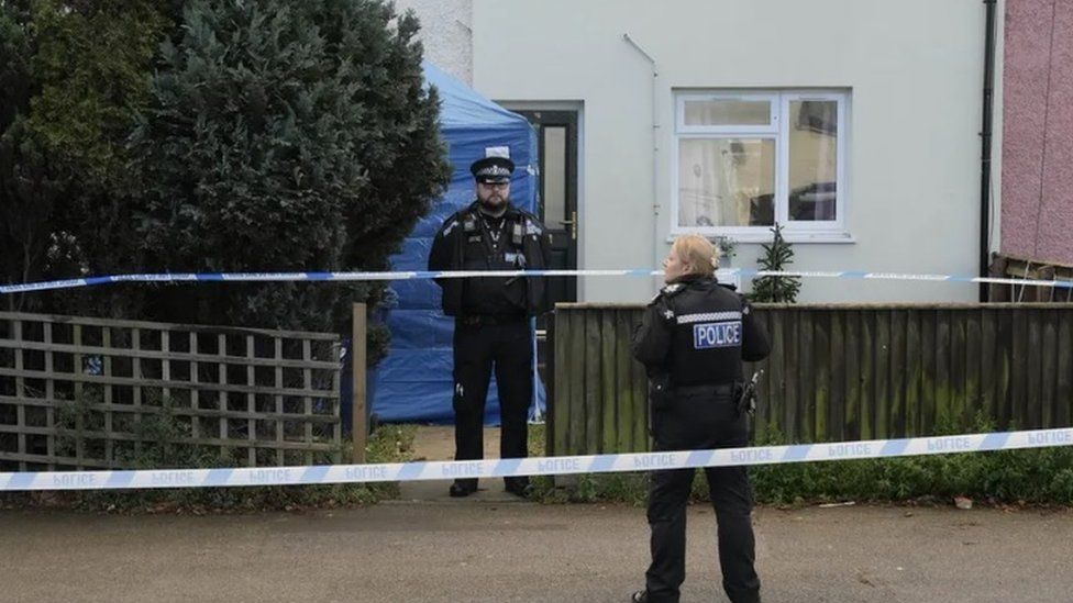 Police officers standing outside an home, blue tent erected in garden