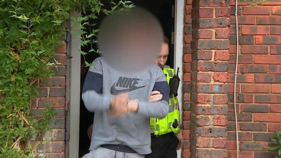 Arrested man being lead out of a house