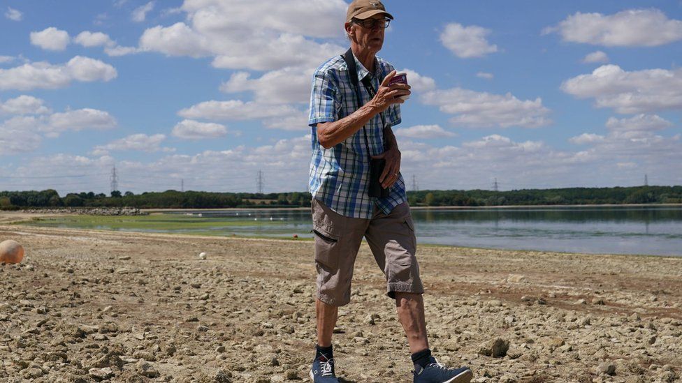 A man walks along dry earth on the banks of a river