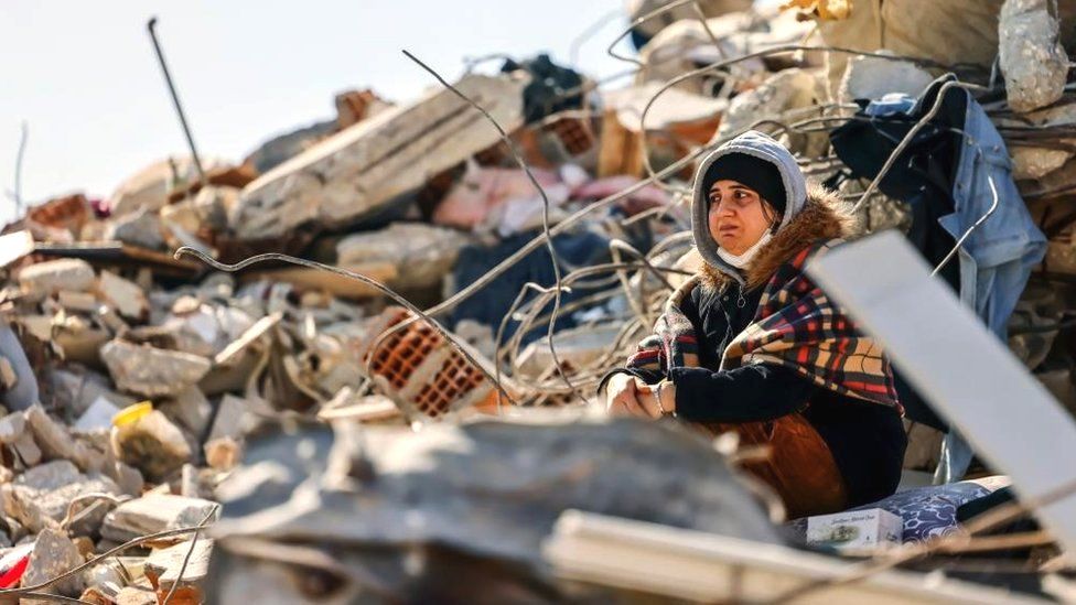 A woman sits among rubble