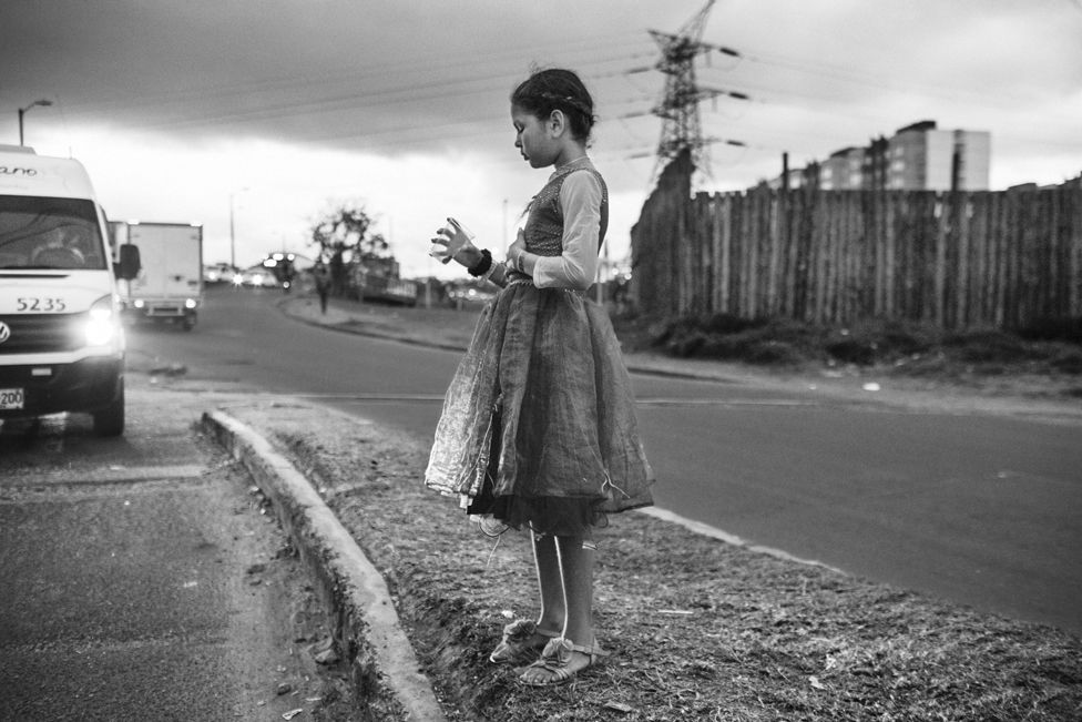 Black and white image of a child standing at the side of a road